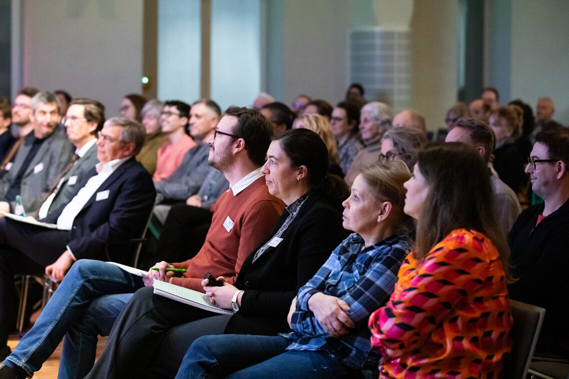 Fachleute sitzen in einem Saal und hören einem Vortrag zu.