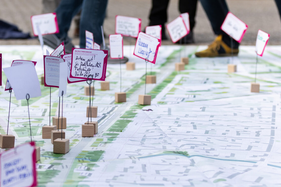 Auf einem großen Plakat stehen kleine Holzständer mit Zetteln auf denen Wünsche und Ideen stehen.