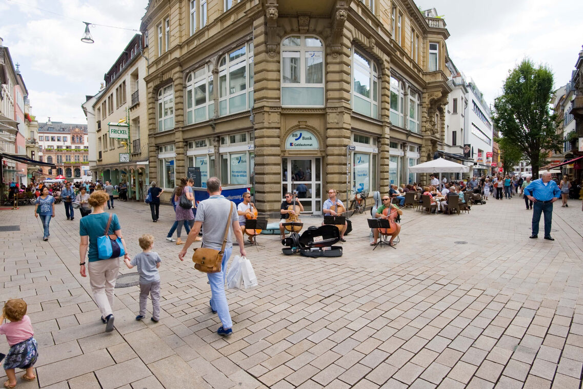 Menschen schlendern durch die Innenstadt und schauen Straßenmusikern zu.