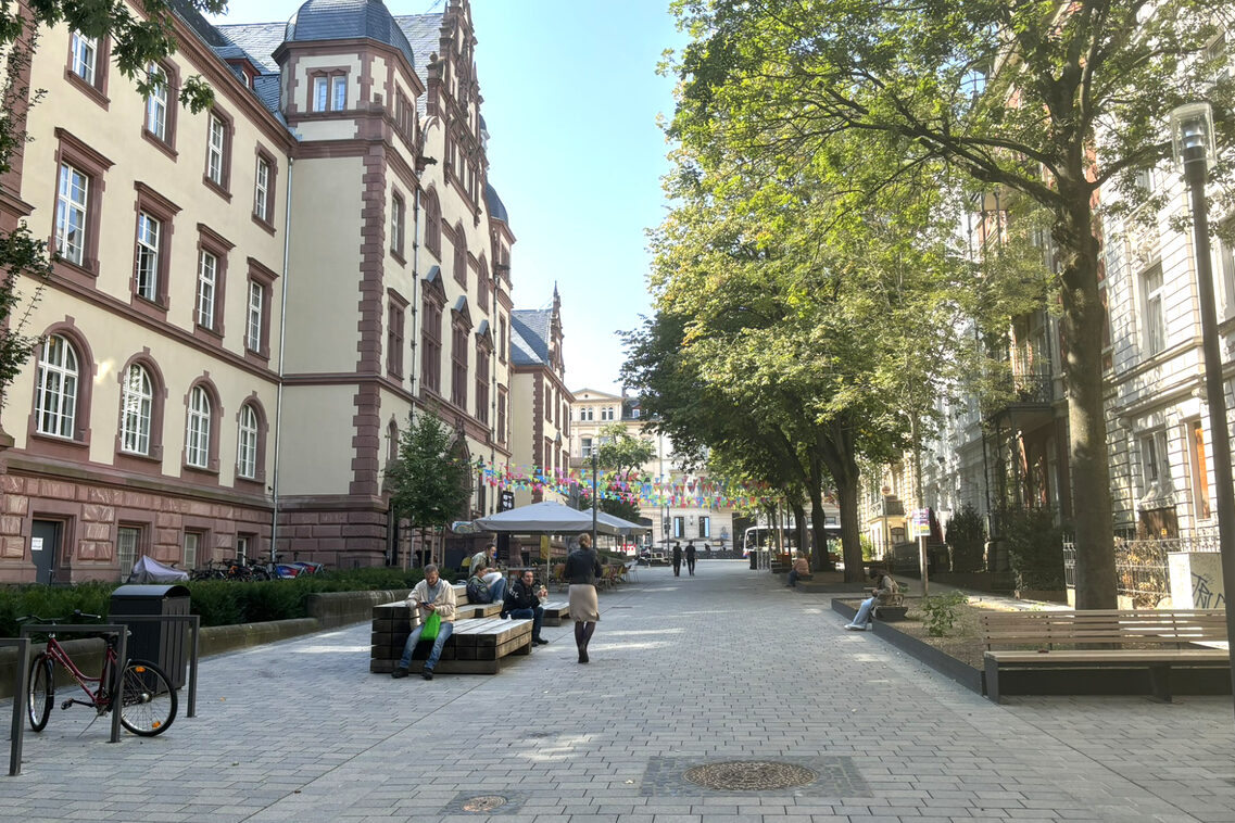Menschen sitzen auf neuen Sitzmöbeln in der neuen Fußgängerzone. Im Hintergrund ist das Alte Gericht und Außengastronomie.