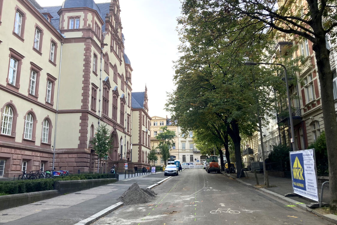 La foto muestra la calle Gerichtsstraße antes de la remodelación en fase de construcción, un coche aparcado delante del patio y una excavadora preparada.