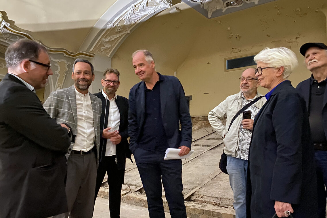 Planer, Beiräte, Vertretende der Politik und der Verwaltung besichtigen das Walhalla. Hier stehen sie im Tribünenbereich.