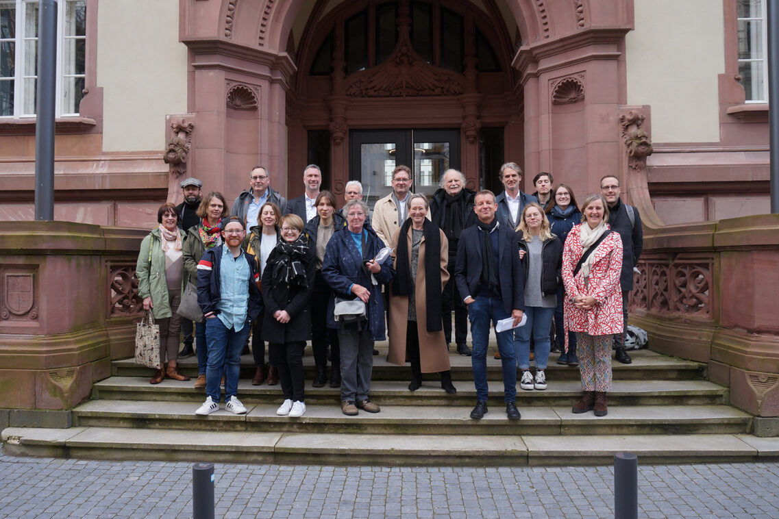 Eine Menschengruppe steht auf den Treppen vor dem Gebäude des alten Gerichts. Die Menschen lächeln in die Kamera.
