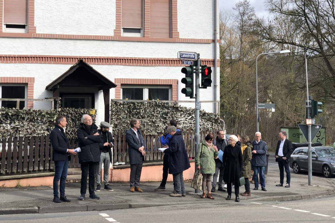 Eine Menschengruppe steht an einer Fußgängerampel auf einem Gehweg.