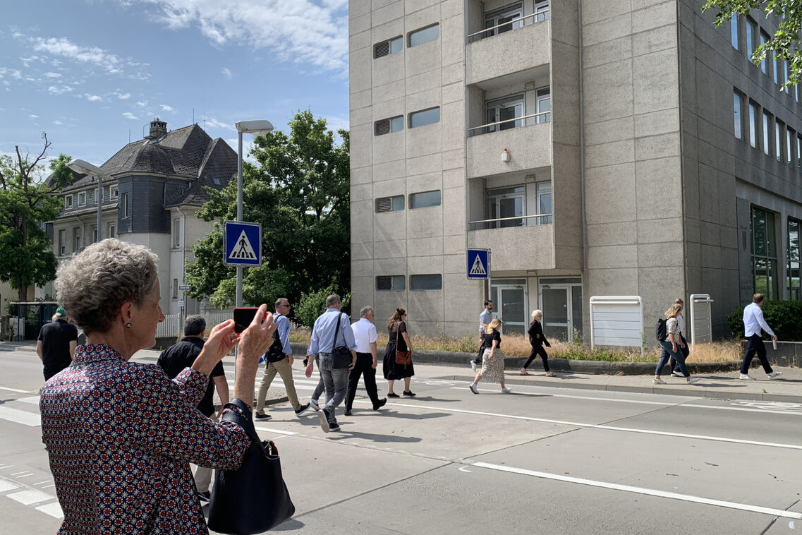 Eine Menschengruppe überquert eine Straße. Eine Frau macht ein Foto.