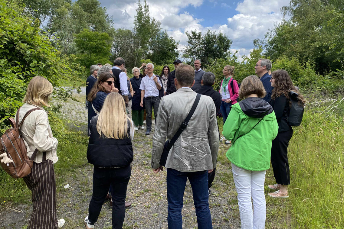 Eine Menschengruppe steht in einem zugewachsenen Grüngelände.