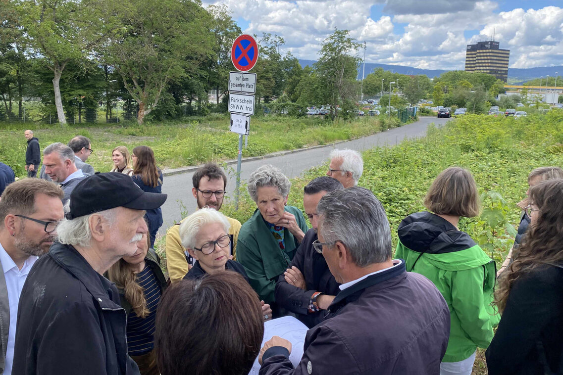 Menschen schauen neben einem zu entwickelnden Parkplatzbereich auf Papiere.
