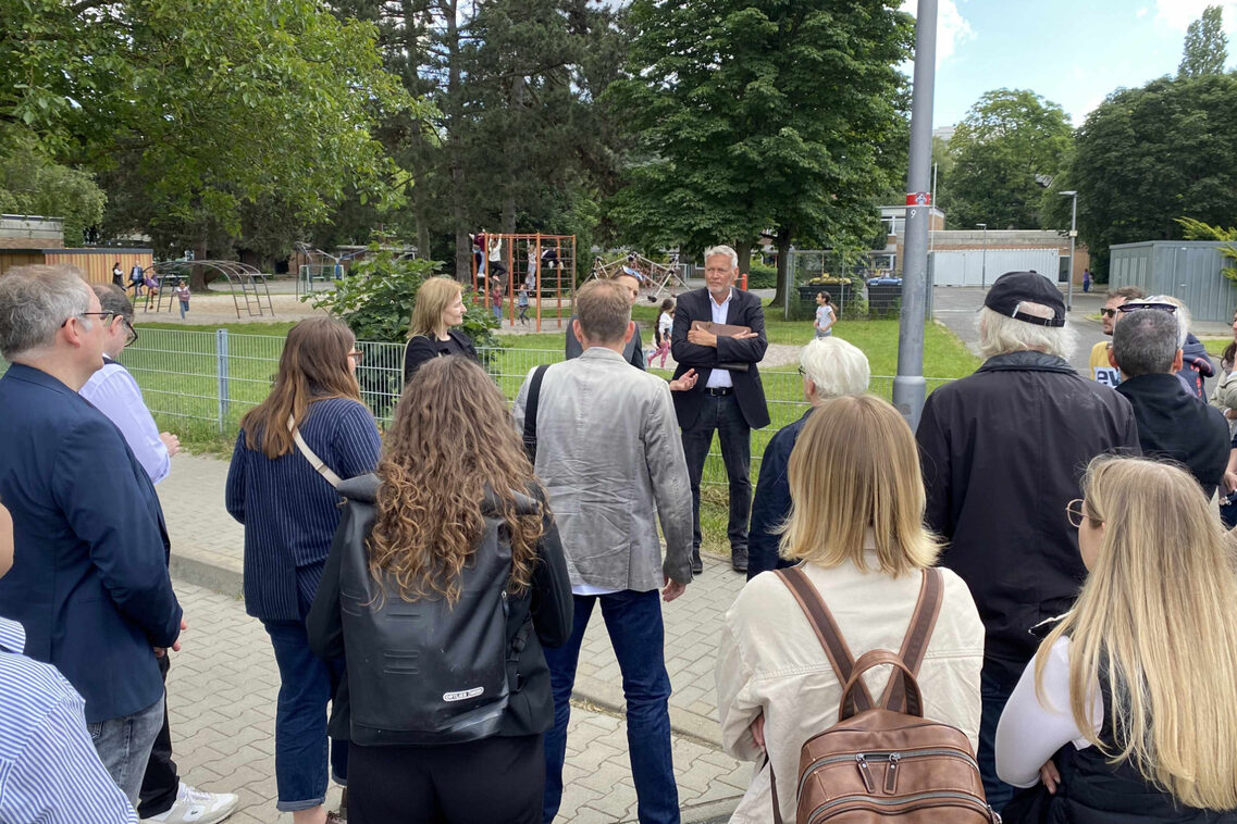 Eine Menschengruppe steht vor dem Spielbereich einer Grundschule.