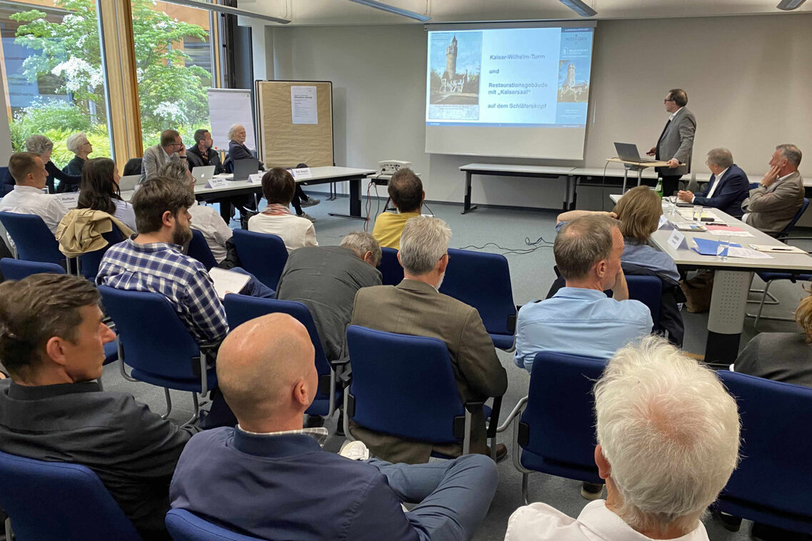 Ein Mann präsentiert dem Beirat und dem Publikum in einer Sitzung historische Türme.