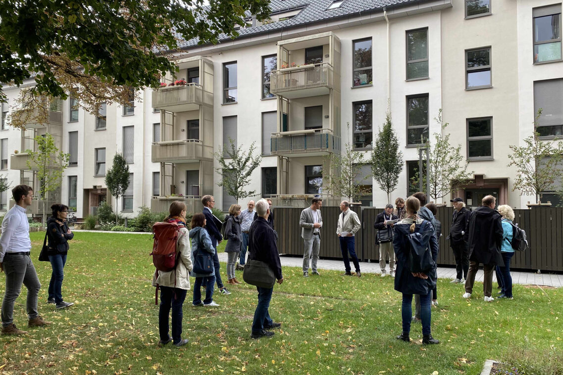 Eine Menschengruppe besichtigt eine neue zukunftsweisende Wohnsiedlung.