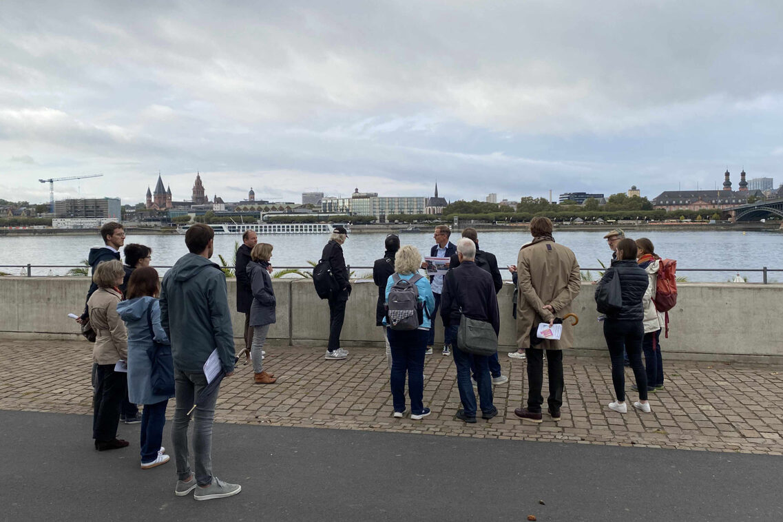 Eine Menschengruppe berät am Rheinufer mit einander.