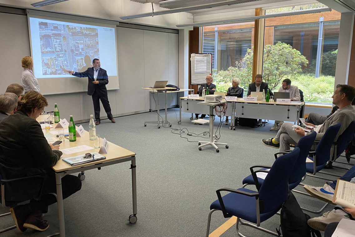 Ein Mann präsentiert in öffentlicher Sitzung Beirat und Publikum ein Vorhaben.