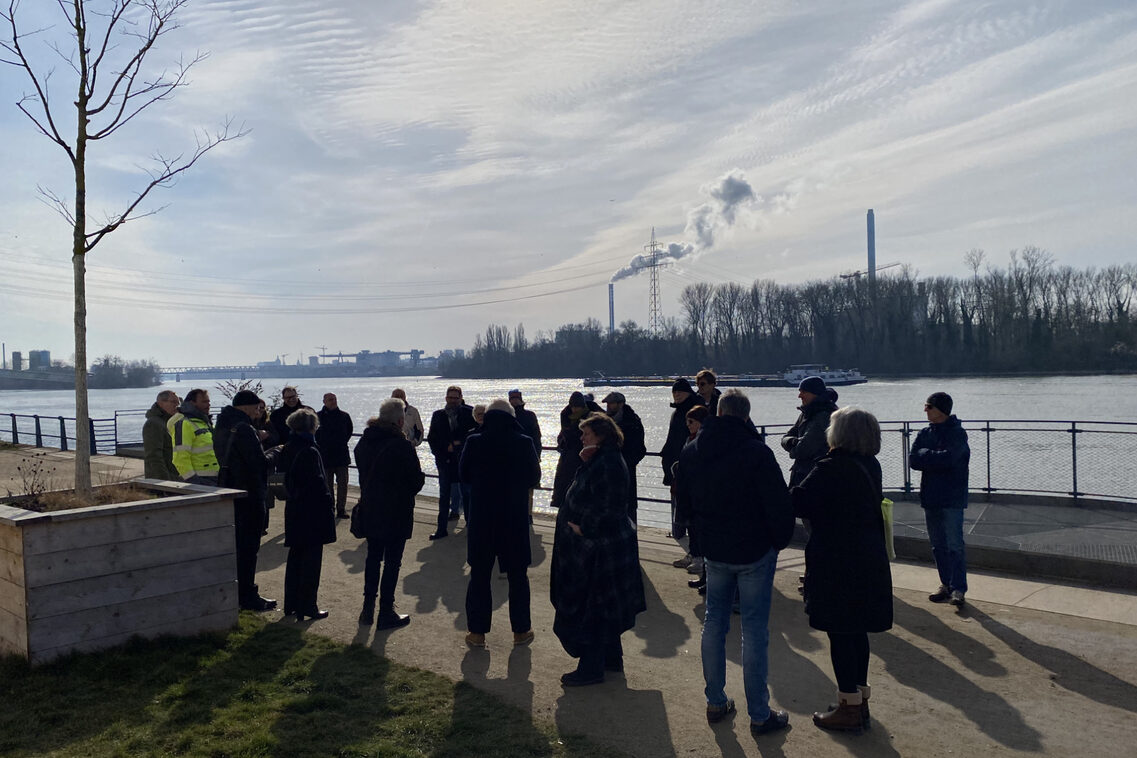 Eine Menschengruppe berät am Rheinufer mit einander.