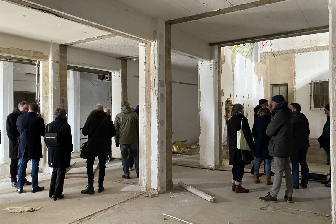 Eine Menschengruppe besichtigt heruntergekommene Innenräume eines Gebäudes.