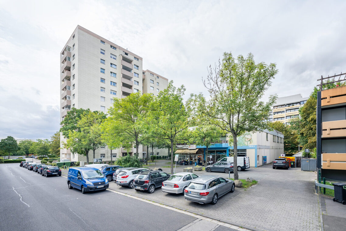 Kleine Ladenzeile mit einem baumgestandenen Platz und parkenden Autos