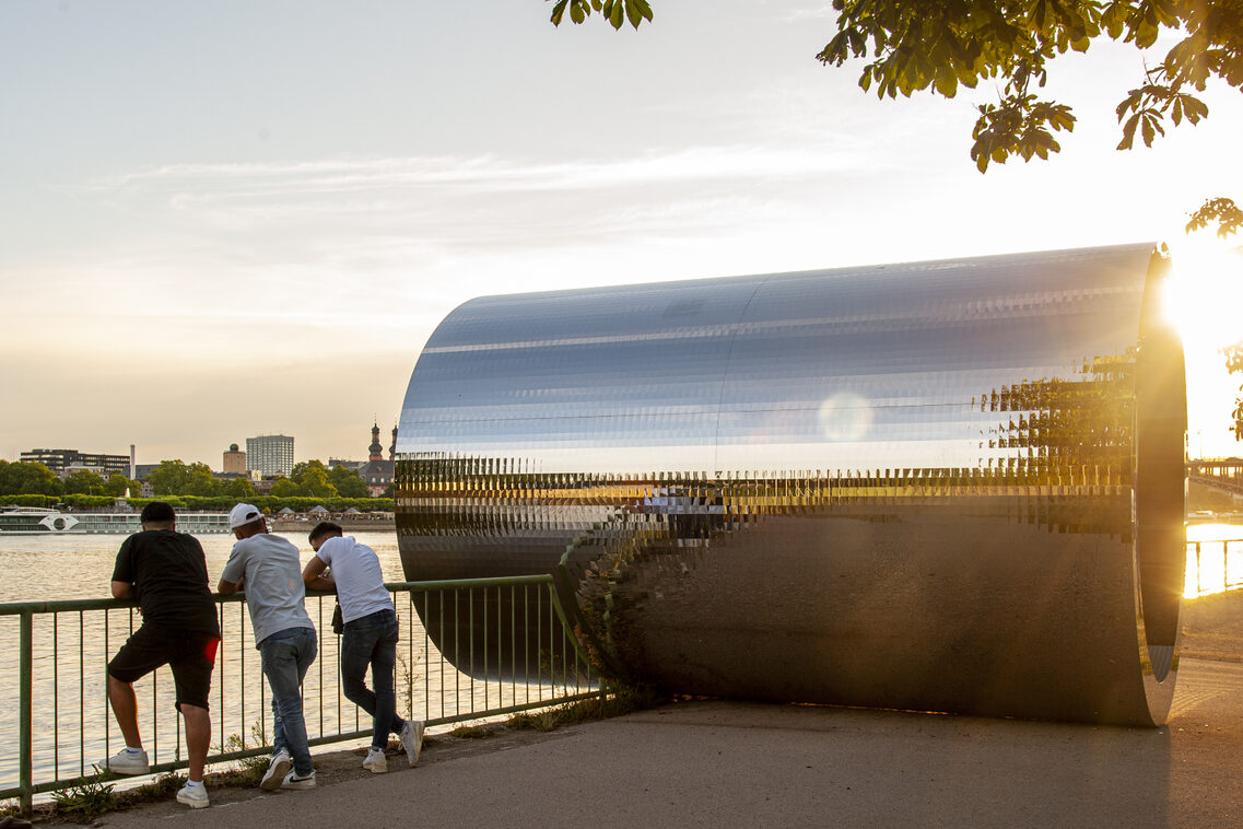 The tube reflects the sunset, while people enjoy the view of the Rhine and Mainz.