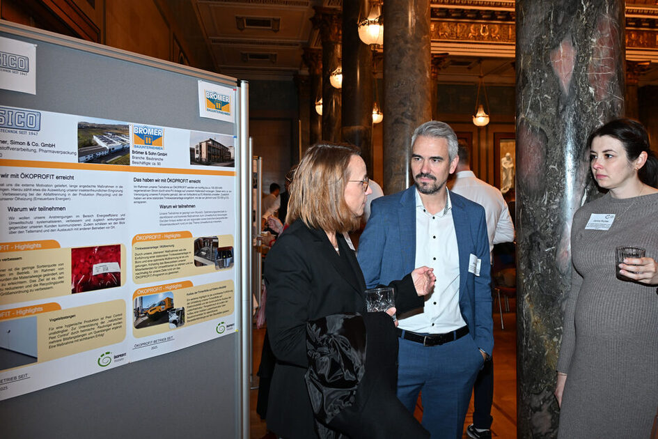 Drei Menschen stehen rechts von einer Informationstafel.