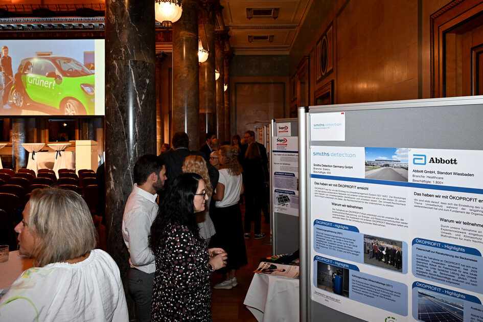 Menschen stehen in einem prunkvollen Raum mit Marmorsäulen vor Informationsständen, einer zeigt das Logo von Abbott und Informationen zu OKOPROFIT.