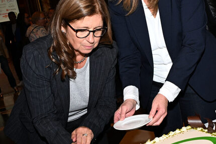 Zwei Frauen in dunklen Anzügen schneiden gemeinsam eine große rechteckige Torte mit der Aufschrift '25 Jahre ÖKOPROFIT WIRTSCHAFT' und grüner Spirale.