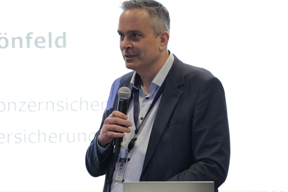 Mann mit grauen Haaren, Anzugjacke und Mikrofon.