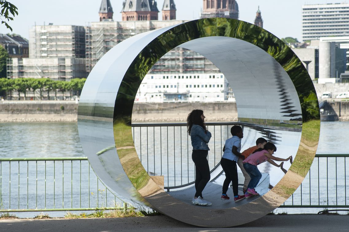 Kinder spielen in der Röhrenskulptur.