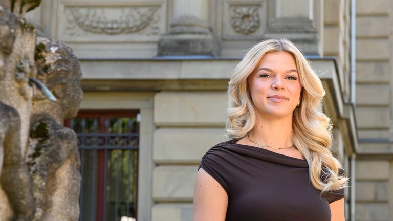 Junge Frau mit blonden Haaren vor historischem Gebäude