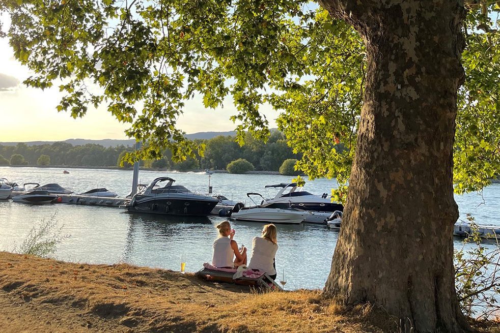 Zwei Frauen sitzen mit einem Getränk am Rhein