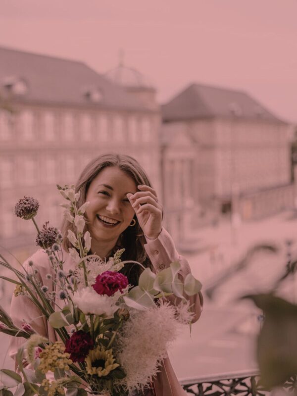 Femeie cu buchet de flori pe un balcon
