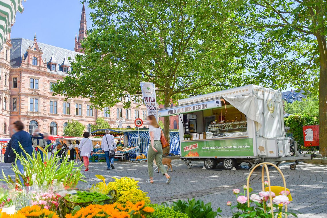 Menschen auf einem Wochenmarkt mit Ständen und historischem Gebäude.
