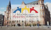 Das Wiesbadener Rathaus im Hintergrund davor das Logo Brücken schlagen Men