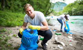 Junger Mann beim Müllsammeln am Ufer eines Flusses
