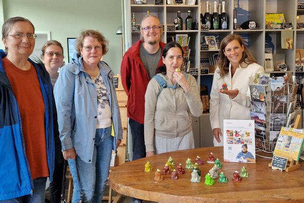 Auf dem Foto sind sechs stehende Menschen vor einem Verkaufstisch in der Wiesbadener Tourist Information zu sehen.
