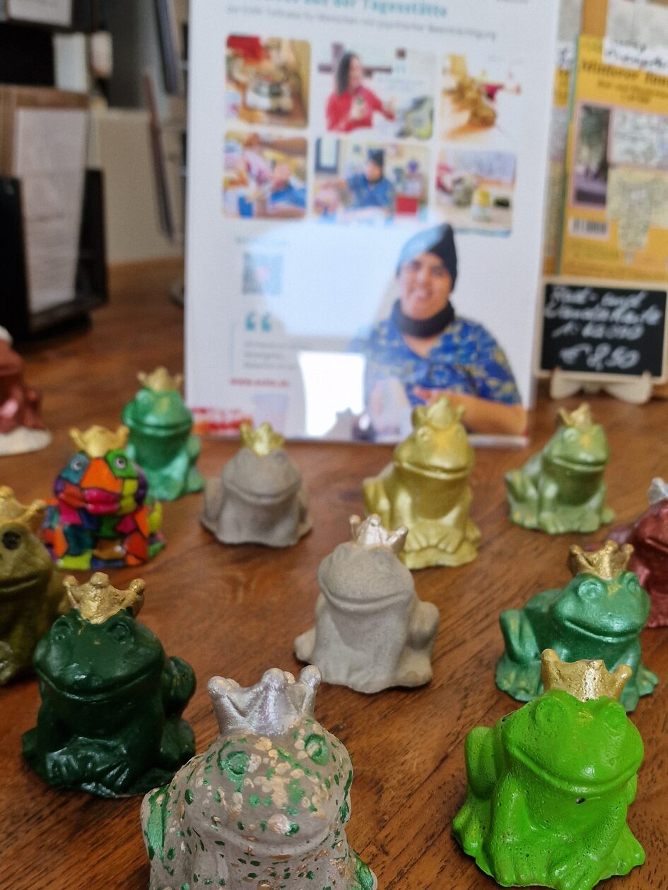Verschieden bemalte Froschfiguren mit Krone aus Ton, die auf einem Holztisch stehen