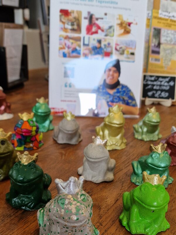 Verschieden bemalte Froschfiguren mit Krone aus Ton, die auf einem Holztisch stehen
