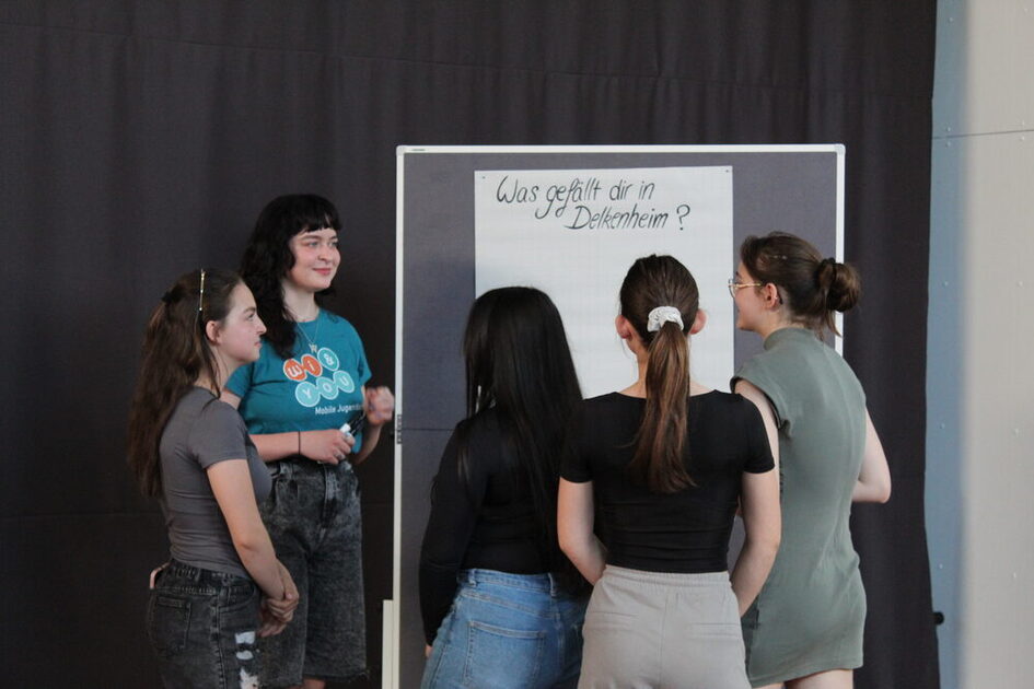 Jugendliche vor einer Pinnwand mit einem Plakat mit der Aufschrift "Was gefällt dir in Delkenheim?".