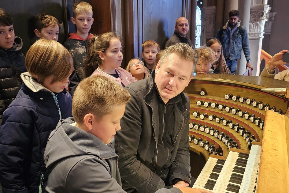 Dr. Thomas Frank sitzt an der Kirchenorgel, umringt von Schülerinnen und Schülern