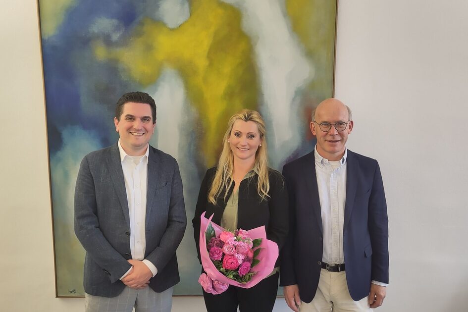 Auf dem Foto sind Kulturdezernent Dr. Hendrik Schmehl, Claudia Hölbling und Jörg-Uwe Funk vor einem Gemälde zu sehen. Frau Hölbling hat einen Blumenstrauß in der Hand.