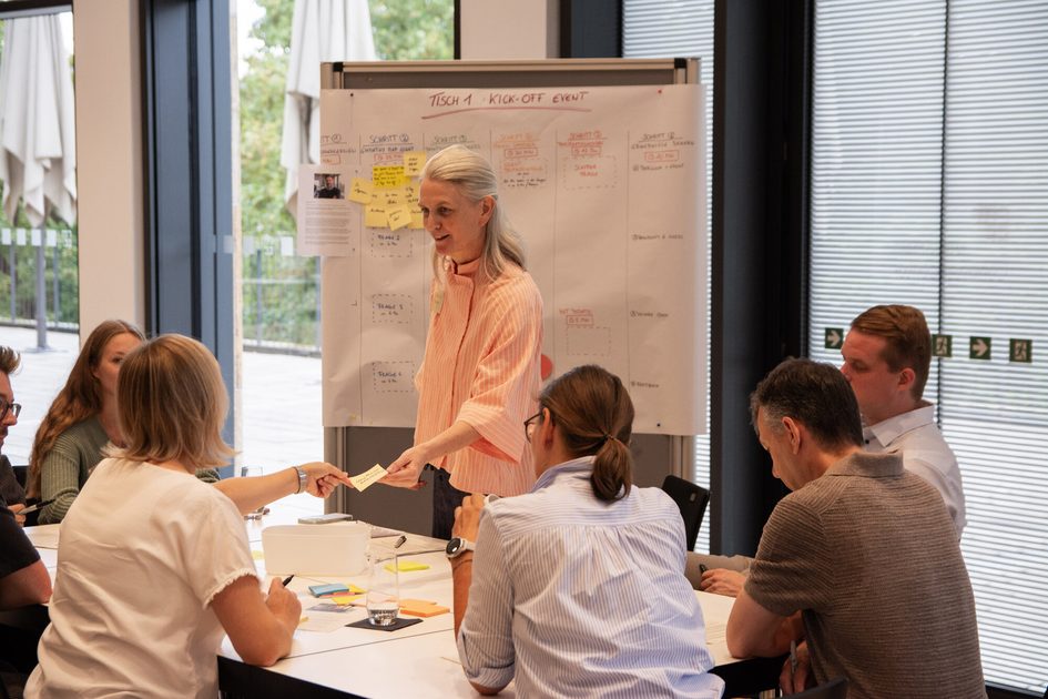 Auf dem Foto sind Menschen bei einem Workshop an einem Tisch zu sehen.