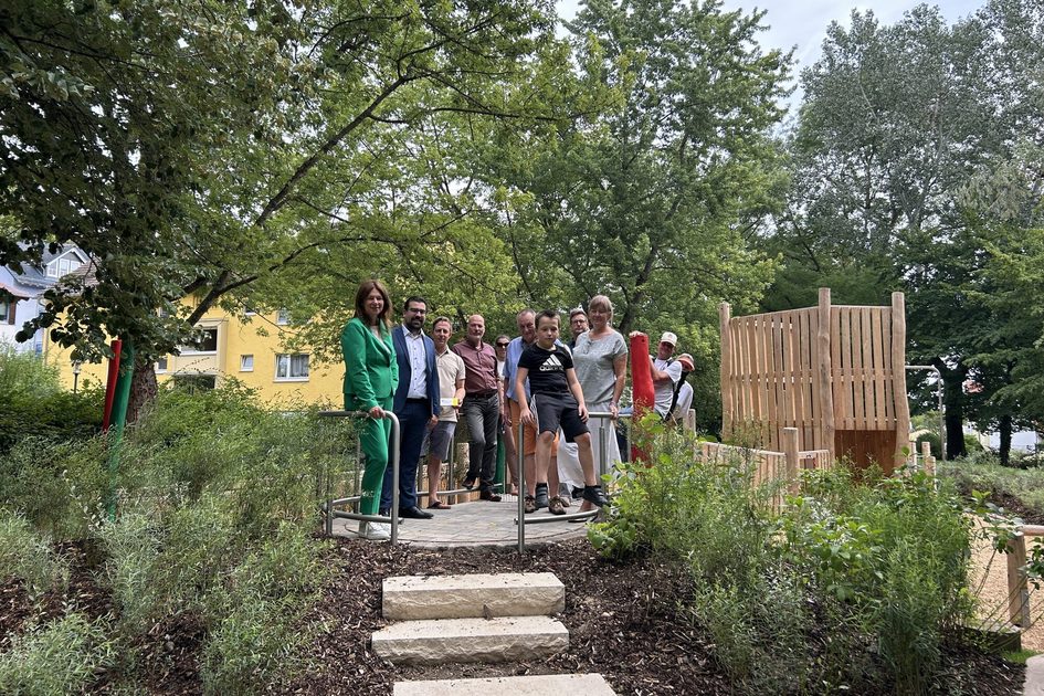 Auf dem Foto sind elf Menschen zu sehen, die auf dem neu gestalteten Spielplatz auf einem Hügel stehen. Im Hintergrund ist ein Klettergerüst zu sehen.