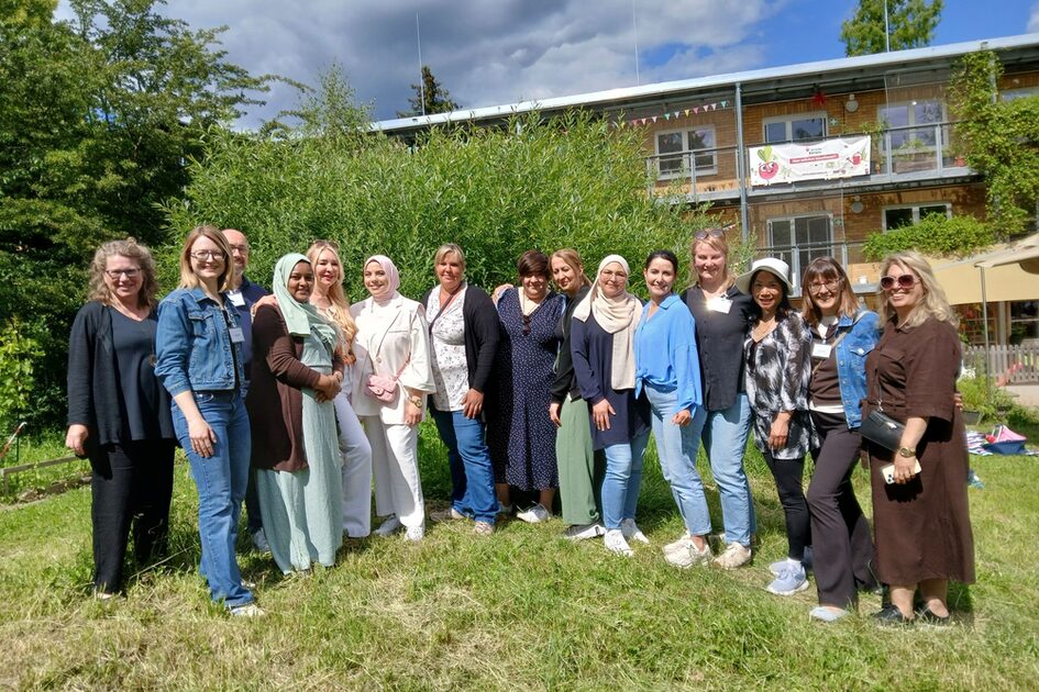 Auf dem Foto sind 14 Frauen und ein Mann zu sehen, die auf einer grünen Wiese vor einem Gebäude stehen.