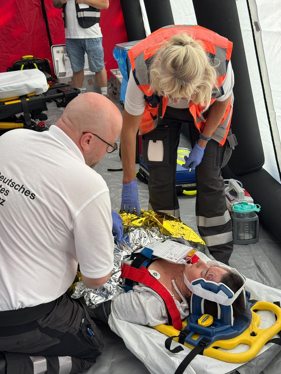 Zwei Einsatzkräfte, die sich in einem Behandlungszelt um eine verletzte Person kümmern.