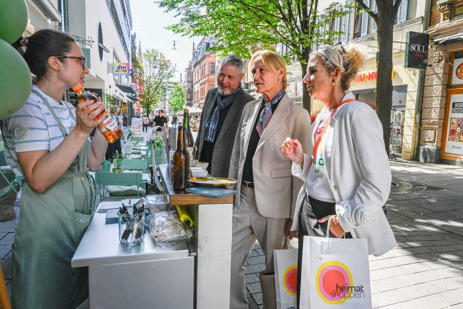 „heimat shoppen“-Rundgang in der Wiesbadener Innenstadt: Daniela Georgi, Wirtschaftsdezernentin, und Sabine Meder, Hauptgeschäftsführerin der IHK Wiesbaden, besuchen mit Citymanager Jens Ackermann das Geschäft „Chez Madlen“ in der Neugasse (Nennung von rechts nach links). Inhaberin Marie Bockstaller berichtet an ihrem Aktionstand über das Angebot ihres Bistros und Feinkostladens.