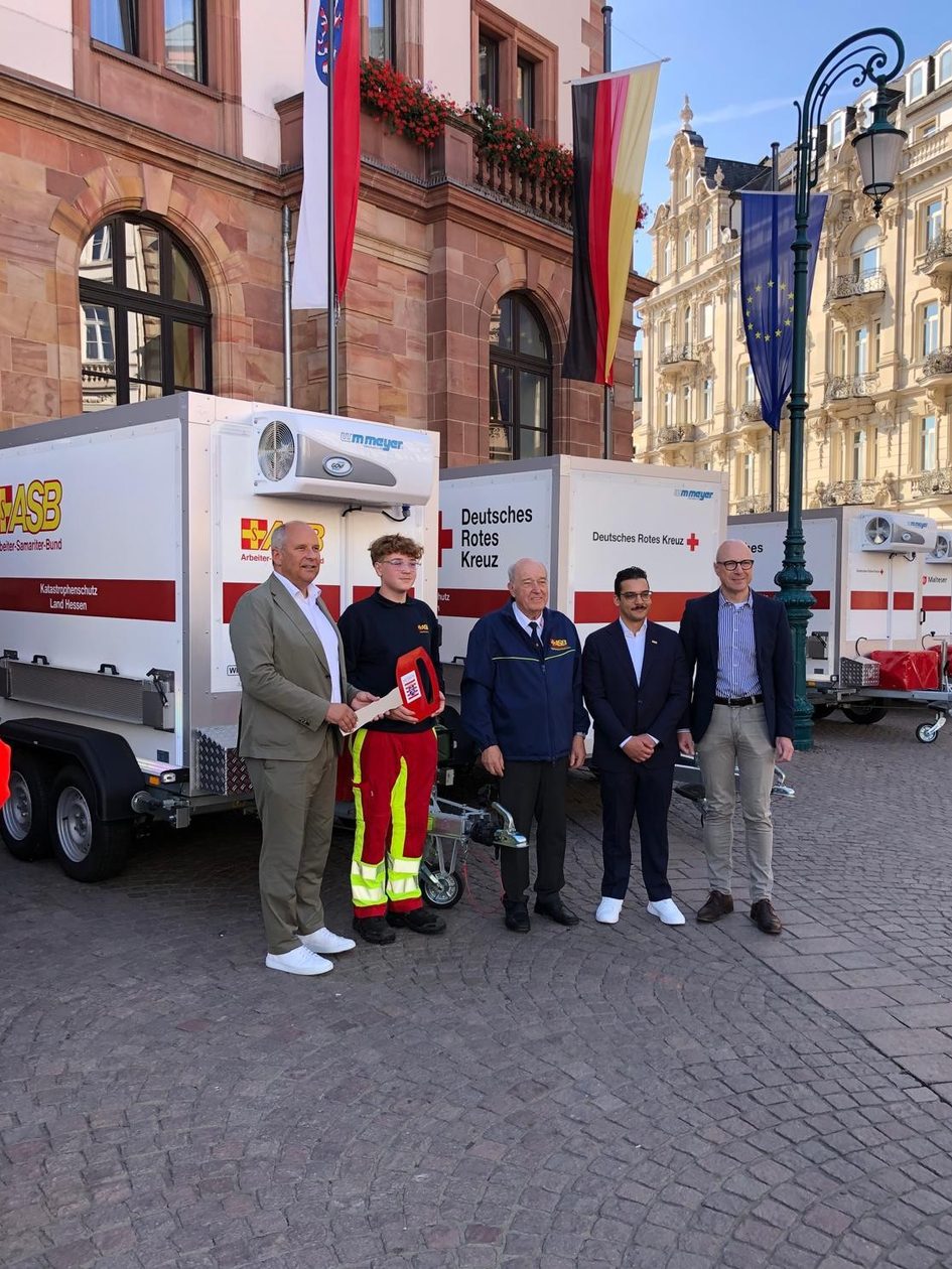 Auf dem Foto sind fünf Herren vor Einsatzfahrzeugen vor dem Wiesbadener Rathaus zu sehen, einer hat einen symbolischen großen Schlüssel in der Hand.