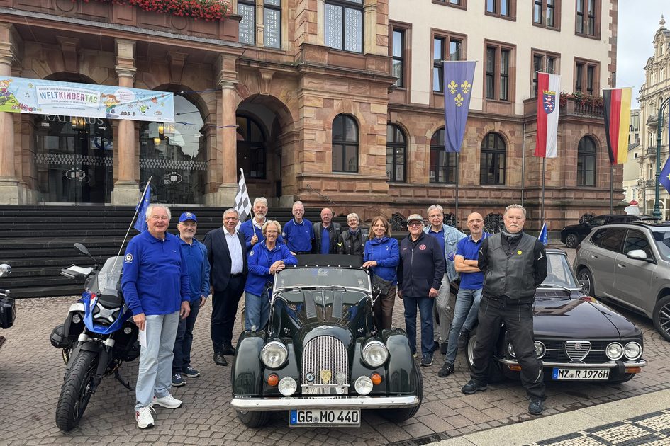 Auf dem Foto sind 13 Personen auf dem Schlossplatz zu sehen, die um ein Oldtimer stehen.