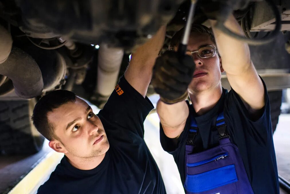 Zwei junge Männer arbeiten unter einem Auto.