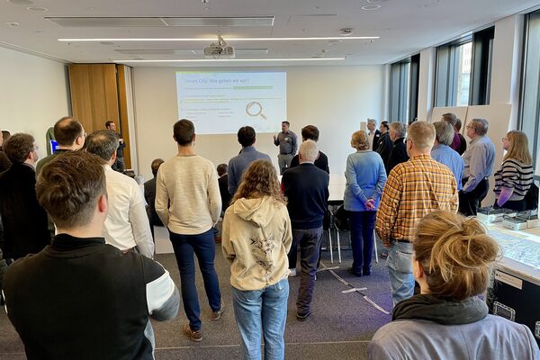 Menschengruppe bei einer Beteiligungsveranstaltung, die einem Vortrag zu Smart City zuhört.