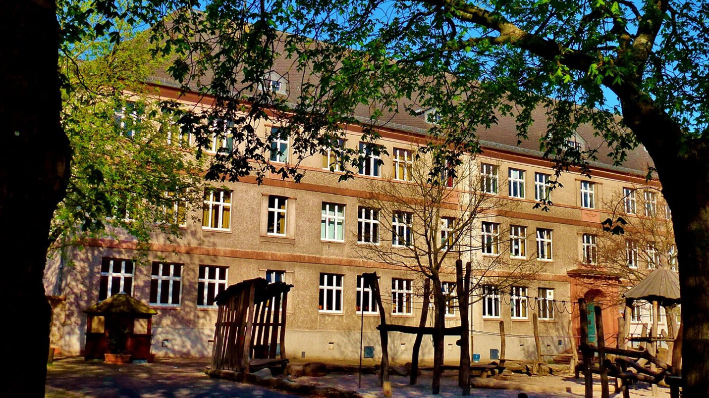 Mittelstufenschule Dichterviertel - historisches Schulgebäude mit Pausenhof und Bäumen.