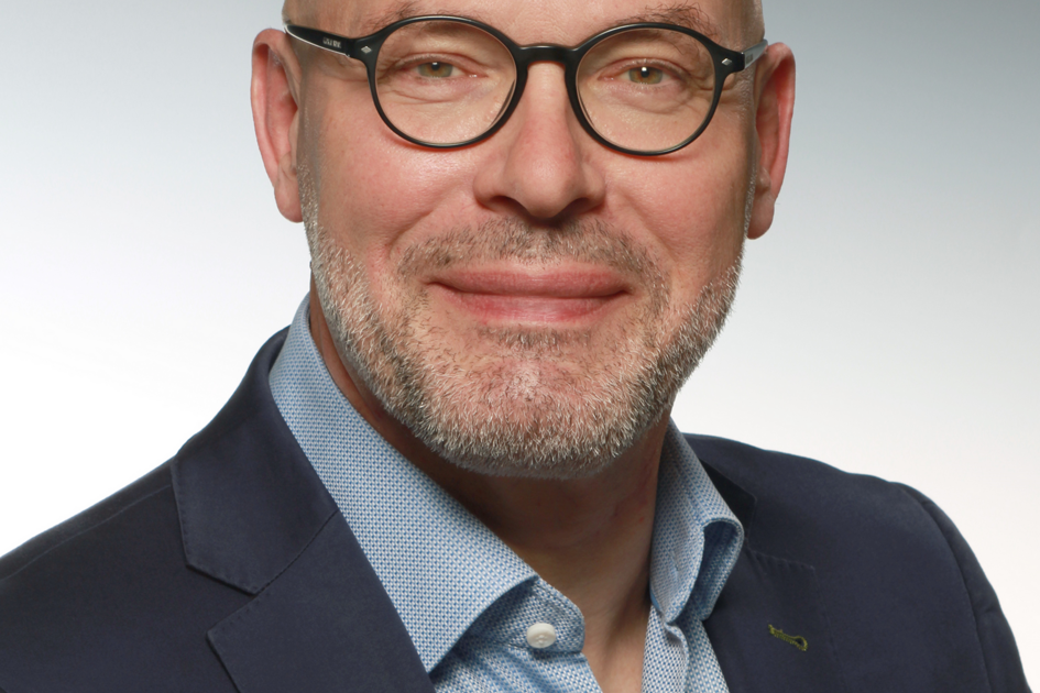 Mann mit kurzen Haaren, Bart und Brille mit Hemd und Jacket.