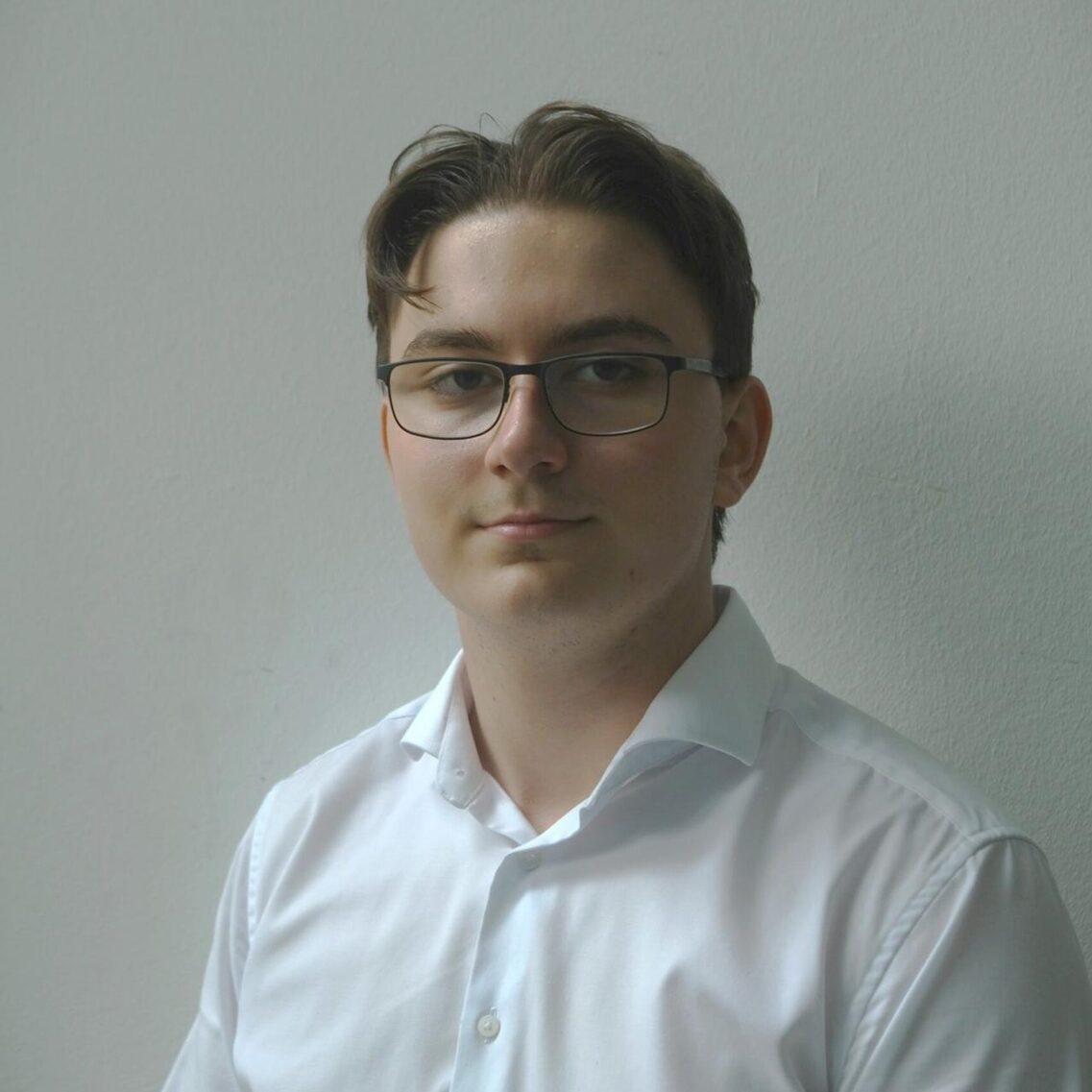 Mężczyzna w okularach i białej koszuli patrzy w kamerę