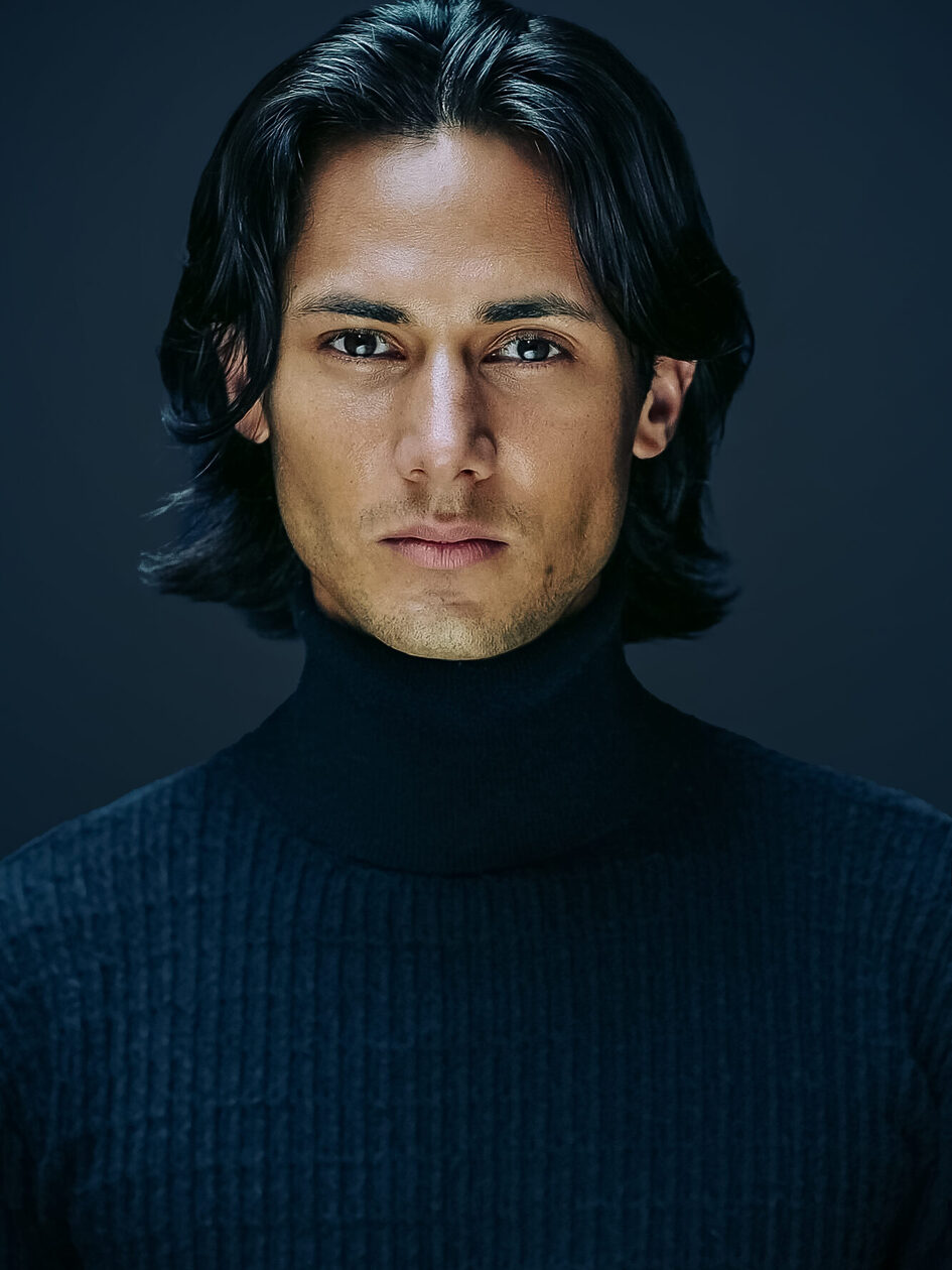 Man with dark turtleneck sweater and half-length dark hair looks into camera
